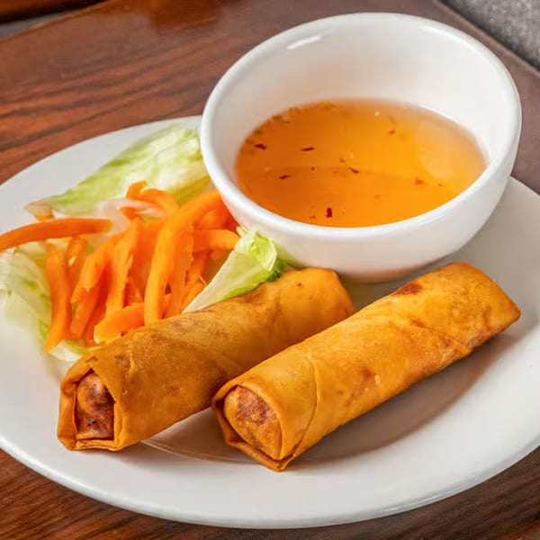 Two crispy Vietnamese spring rolls with lettuce, shredded carrots, and a side of dipping sauce.