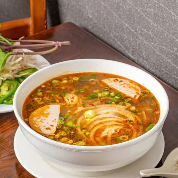 A bowl of Anise Viet Cuisine's spicy Vietnamese noodle soup with sliced pork and green onions.