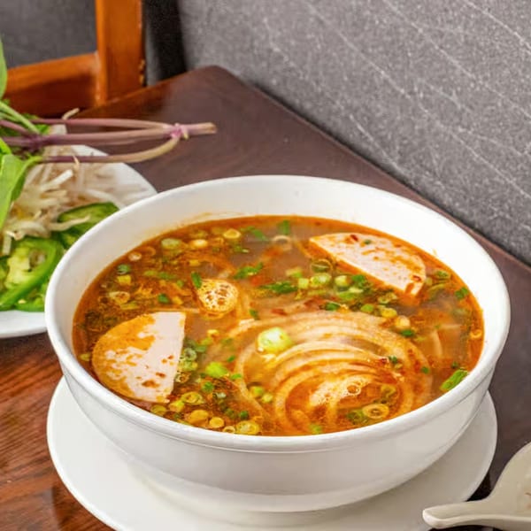 A steaming bowl of Vietnamese bun bo hue soup with noodles, meat, and green onions.