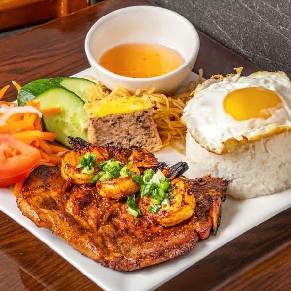 Vietnamese grilled pork chop and shrimp with rice, fried egg, and pickled vegetables on a white plate.