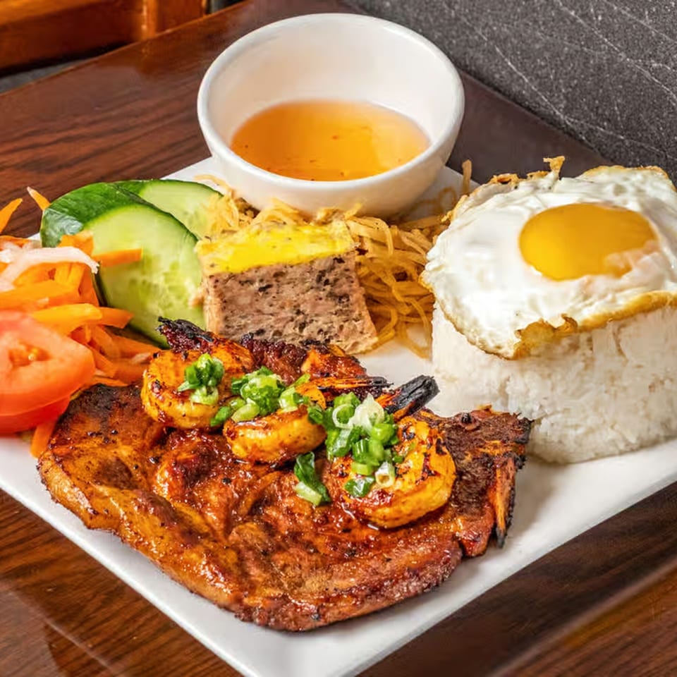 Vietnamese grilled pork chop and shrimp with rice, fried egg, and pickled vegetables on a white plate.