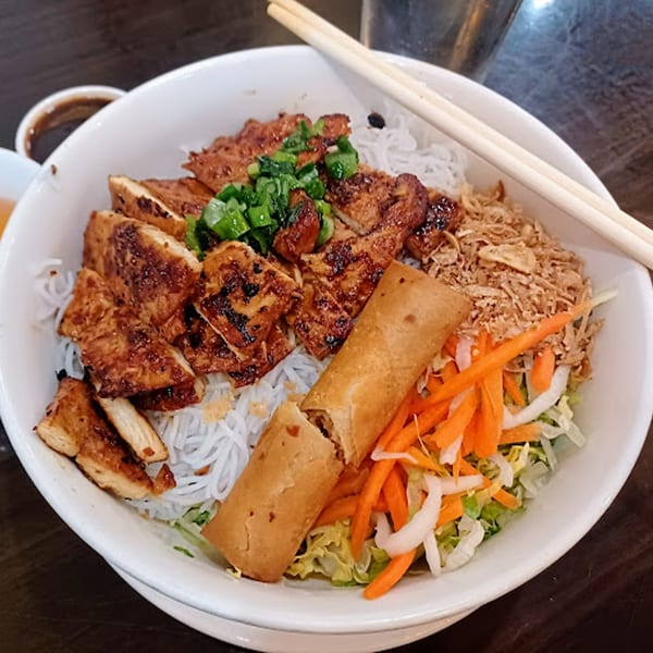 A Vietnamese vermicelli bowl with grilled chicken, spring roll, fresh vegetables, and fried shallots.